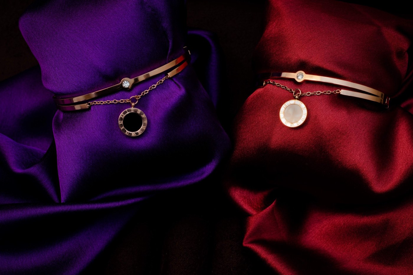 Two rose-gold charm bracelets resting on violet and crimson satin